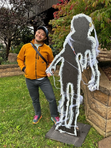 person with bright jacket and pants stands outside next to a spooky statue